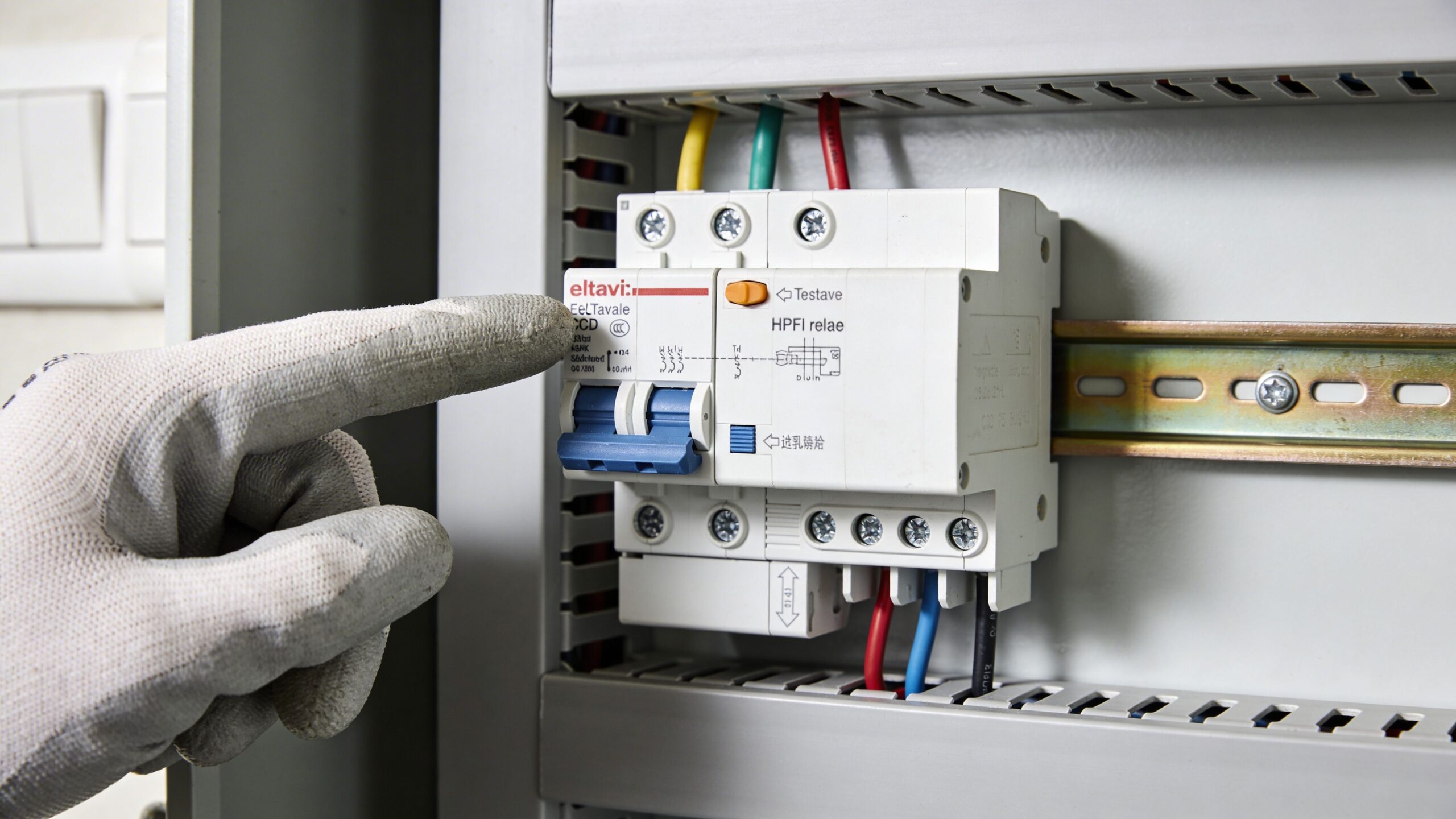 En hånd i en arbejdshandske peger på et HPFI-relæ monteret i et elskab til boliginstallationer.