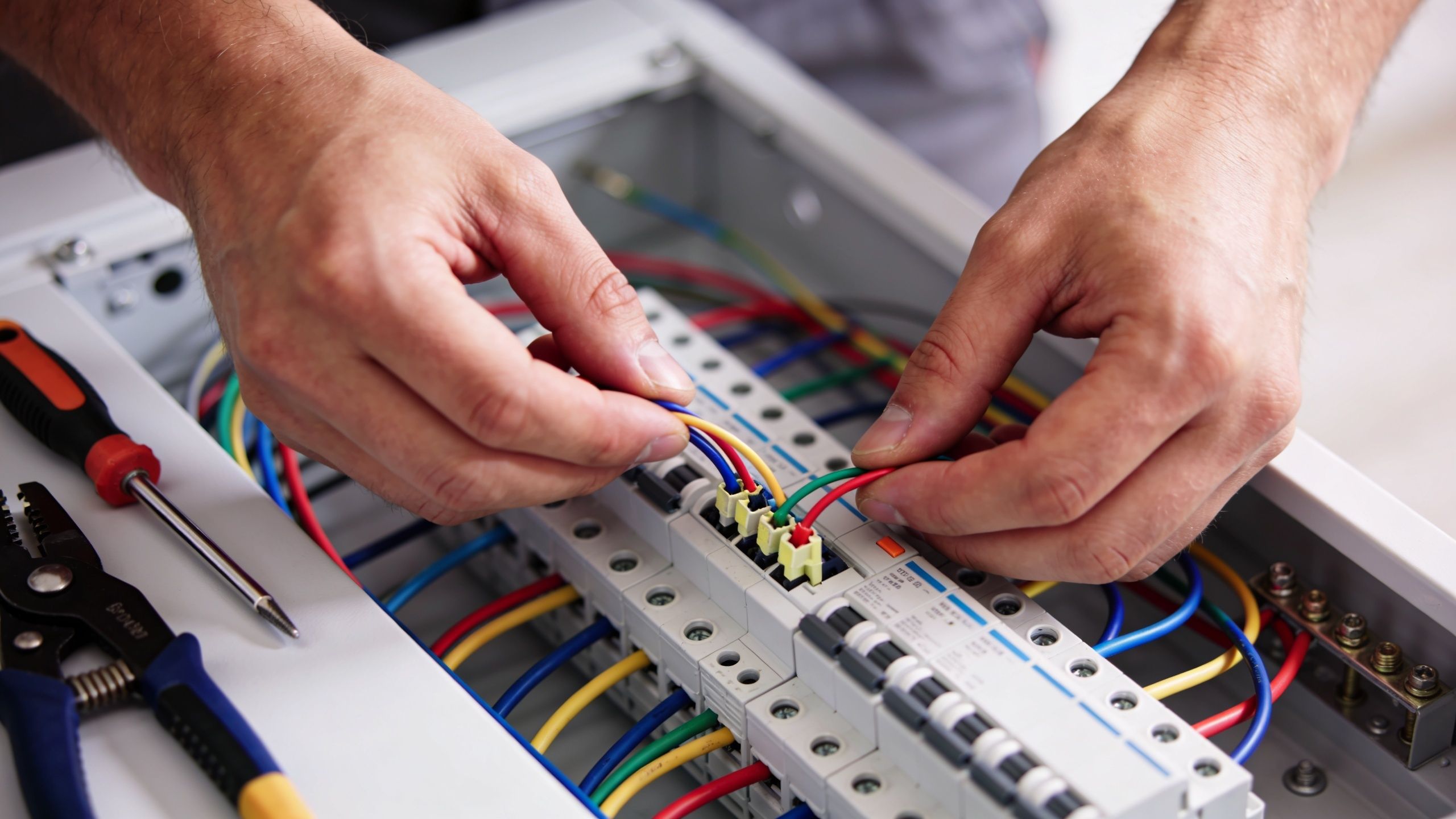 En elektriker arbejder fokuseret på at tilslutte elektriske ledninger i en sikringsboks med professionelt værktøj tæt på.