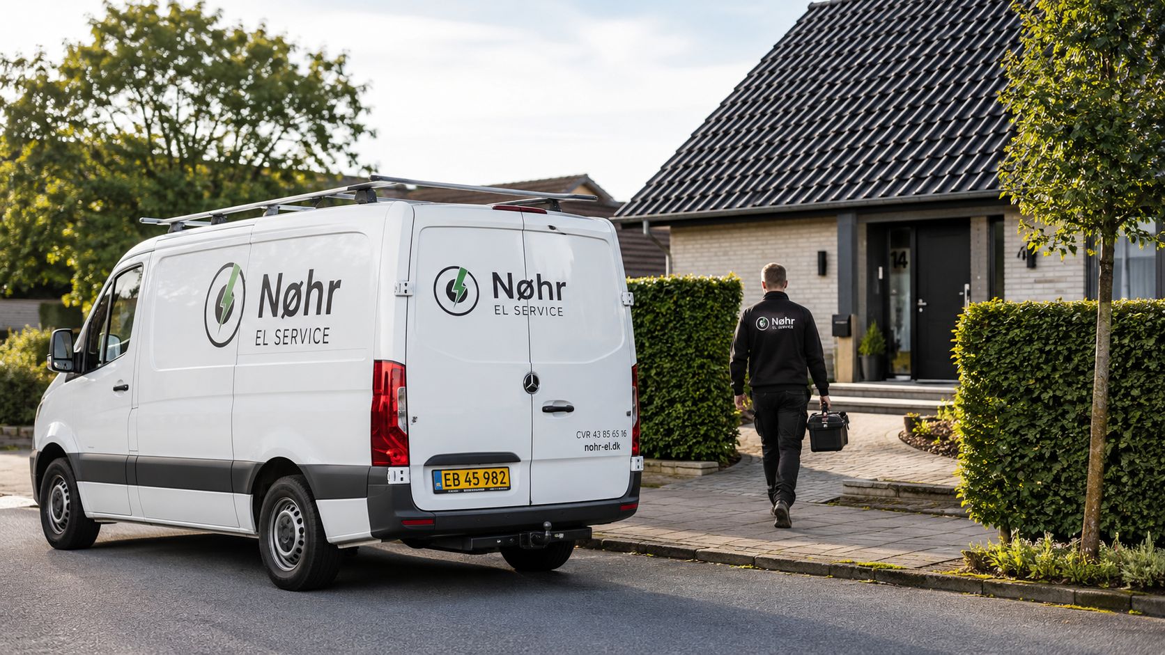 En medarbejder fra Nøhr El Service går mod en bolig med værktøjskasse, mens firmabilen holder parkeret ved vejen.