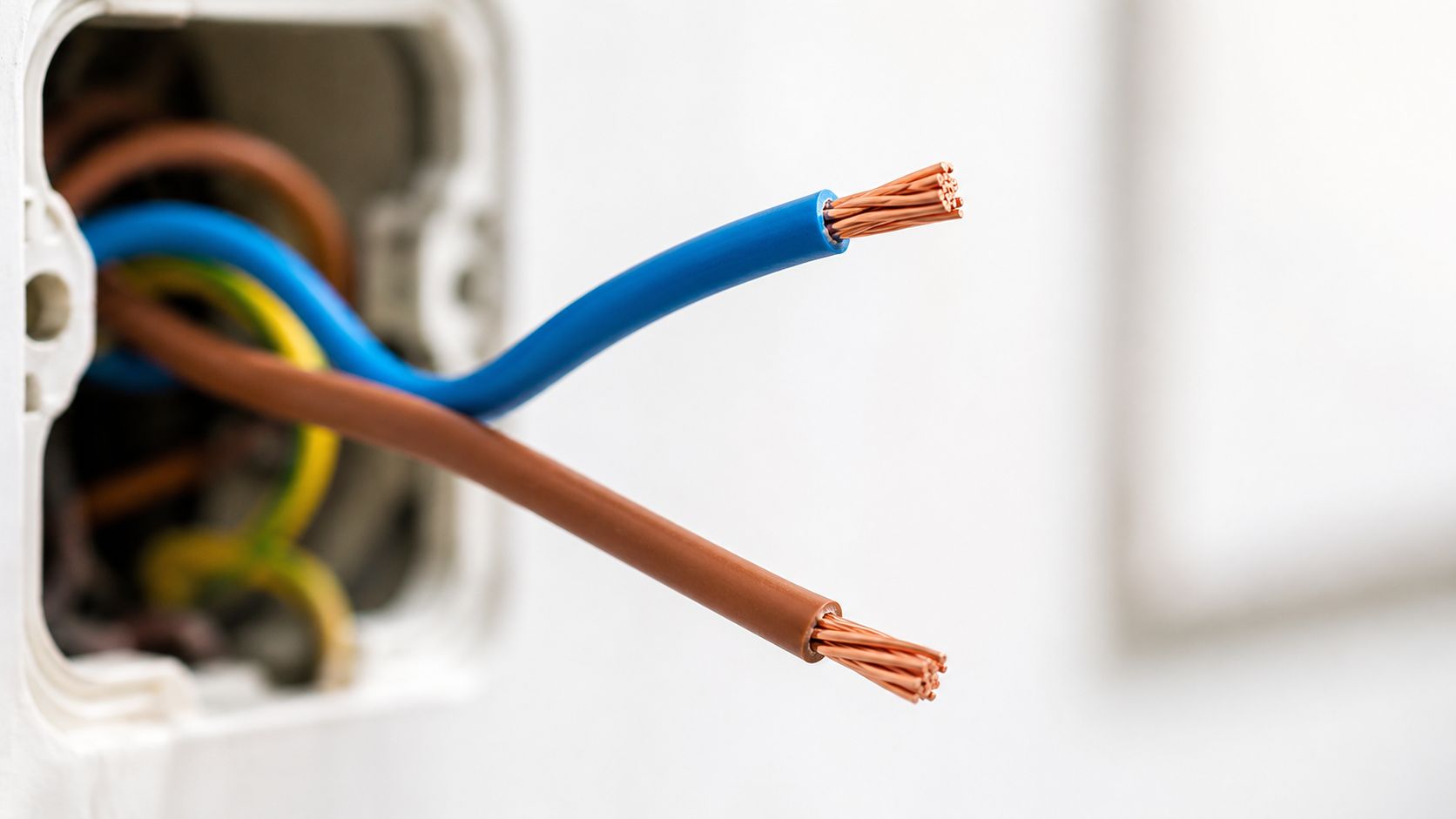 Nærbillede af elektriske ledninger i en vægdåse med synlige kobbertråde til el-installation i et hjem.