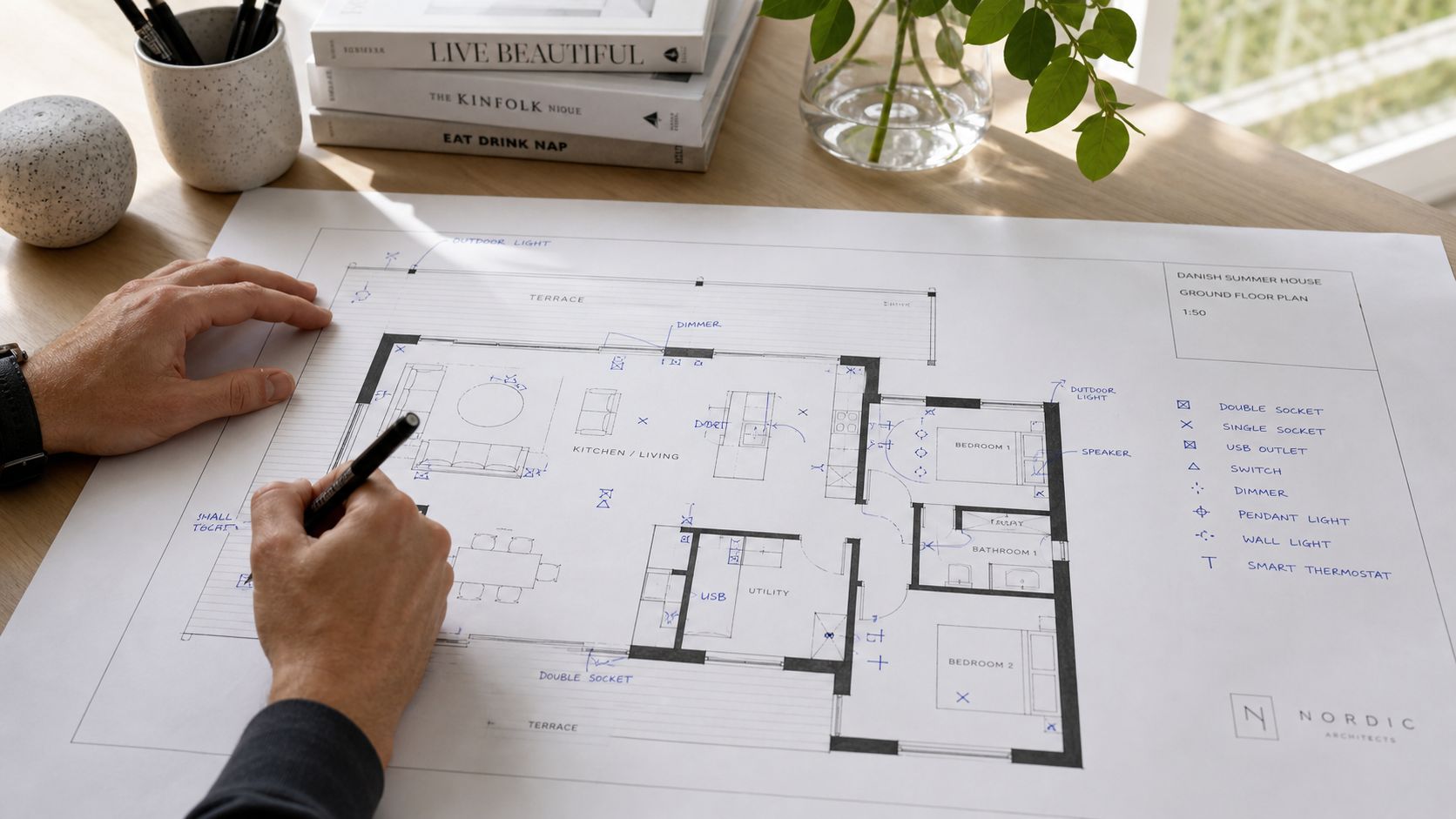 En arkitekt arbejder med en skitse af en grundplan til et moderne sommerhus på et skrivebord.
